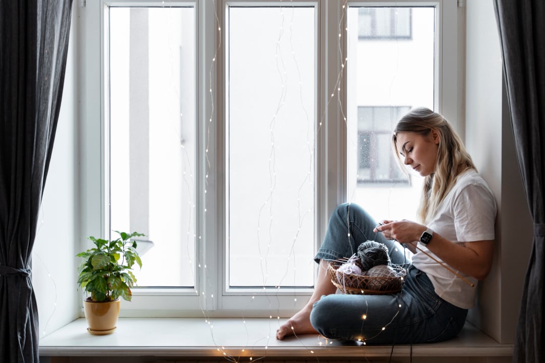 mujer tejiendo junto a la ventana blanca pvc con persiana enrollable subida instalacion de persianas la Enrollada a Coruna